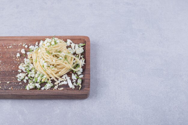 Sabrosos espaguetis hervidos con queso rallado sobre tabla de madera.