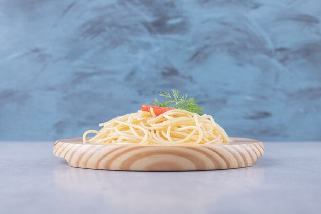 Sabrosos espaguetis hervidos con tomates en placa de madera.