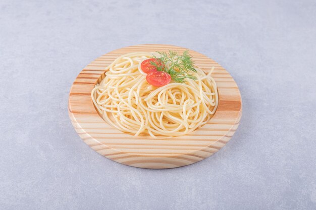 Sabrosos espaguetis hervidos con tomates en placa de madera.