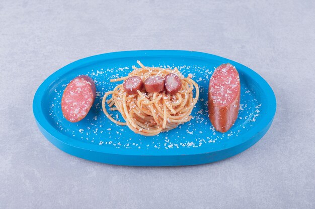Sabrosos espaguetis con salchichas en placa azul.