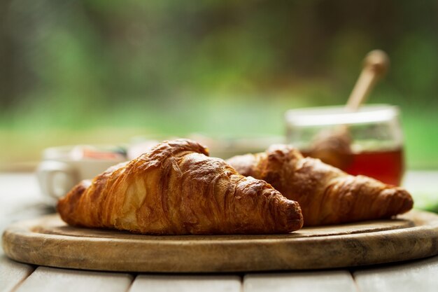 Sabrosos hermosos cruasanes en tabla de madera. Desayuno continental tradicional. Granola con frutas y miel en el fondo.