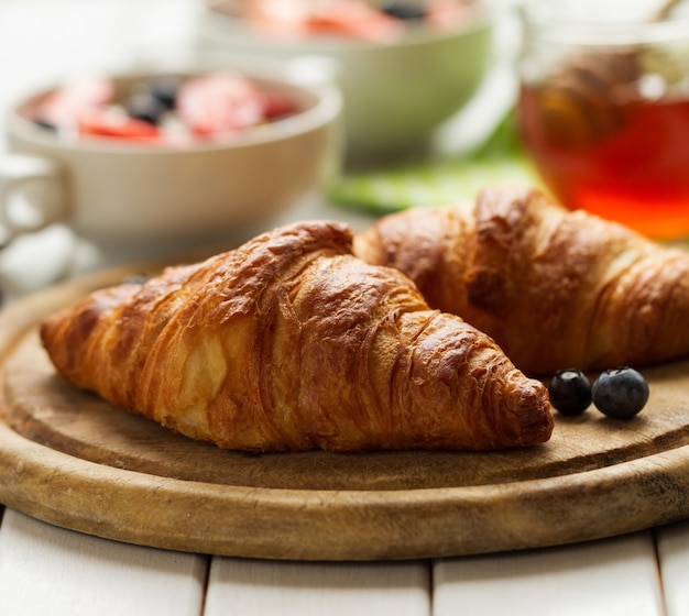 Sabrosos hermosos cruasanes en tabla de madera. Desayuno continental tradicional. Granola con frutas y miel en el fondo.