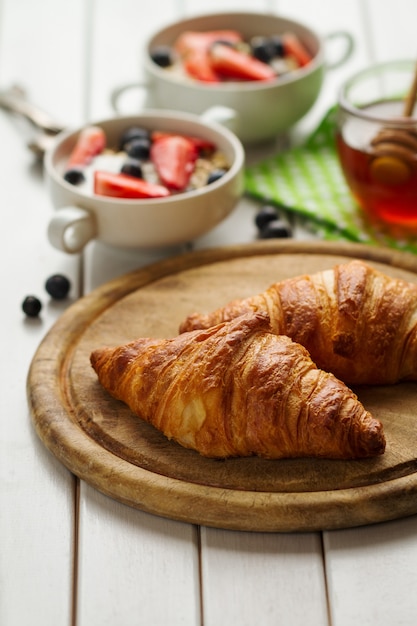 Sabrosos hermosos cruasanes en tabla de madera. desayuno continental tradicional. granola con frutas y miel en el fondo.