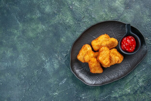 Sabrosos nuggets de pollo y salsa de tomate en placa negra en el lado izquierdo sobre una superficie oscura