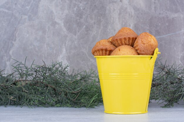 Sabrosos pasteles pequeños en cubo amarillo con rama de pino.