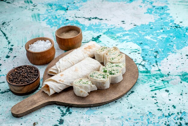 Sabrosos rollos de verduras enteras y en rodajas con verduras y condimentos en un escritorio azul brillante