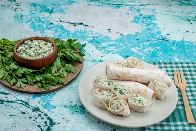 Sabrosos rollos de verduras enteras y en rodajas con verduras y ensalada en el escritorio azul