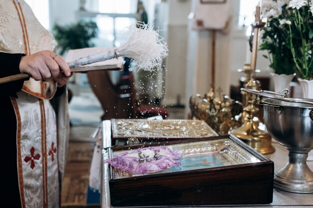 Sacerdote está rociando agua bendita en los anillos de boda en la iglesia