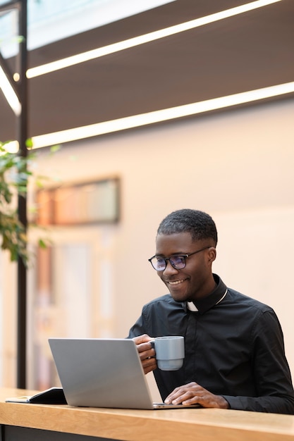 Sacerdote masculino joven que usa la computadora portátil en un café