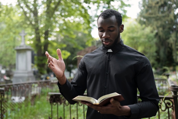 Foto gratuita sacerdote masculino leyendo la biblia en el cementerio