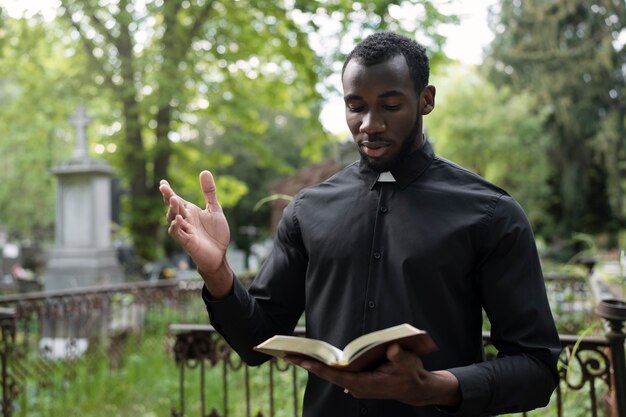Sacerdote masculino leyendo la biblia en el cementerio