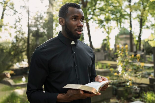 Sacerdote masculino leyendo de la biblia en la tumba con familia de luto