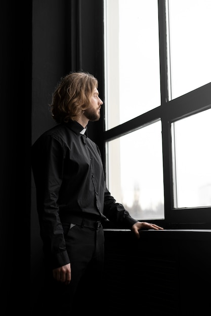 Foto gratuita sacerdote de tiro medio mirando por la ventana.