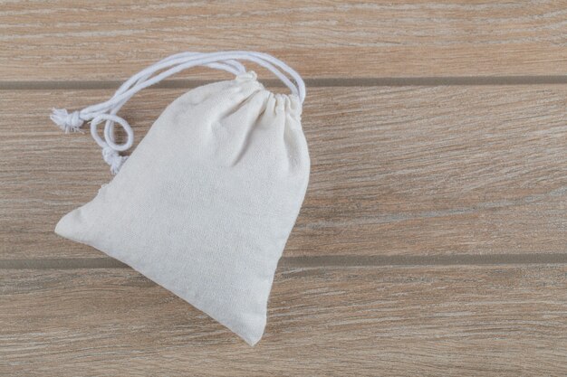 Saco blanco cerrado lleno de granos de maíz sobre una mesa de madera.