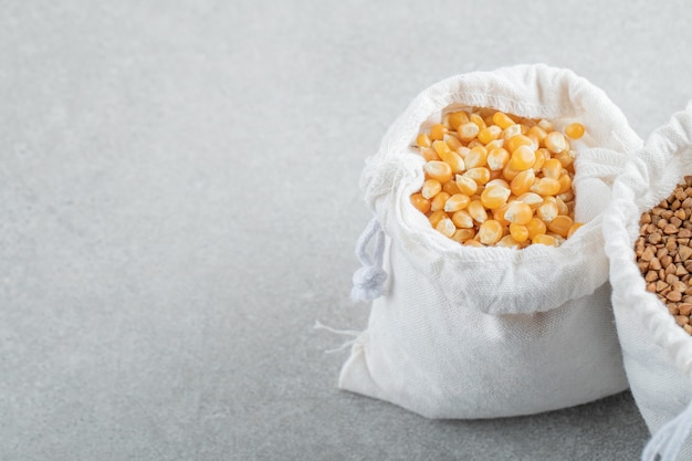 Foto gratuita un saco blanco lleno de granos de maíz y trigo sarraceno sobre un fondo de mármol.
