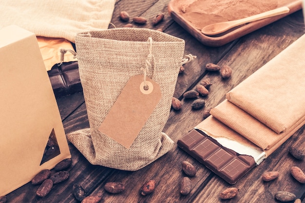 Saco de granos de cacao con pila de barras de chocolate en la mesa de madera