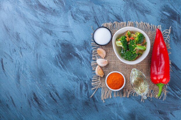 Sal, especias, aceite, verduras y sopa de pollo sobre una arpillera sobre la superficie azul