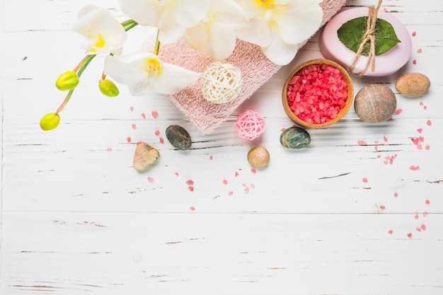 Sal; jabón; piedras de spa; Toalla y flores en superficie de madera.