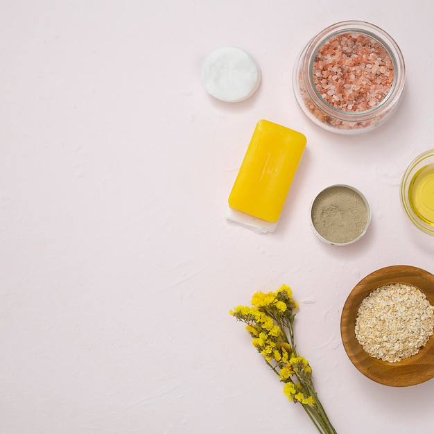 Sal de roca; almohadillas de algodón; jabón; avena; Flores de limonium amarillas y productos cosméticos en superficies de concreto blancas.