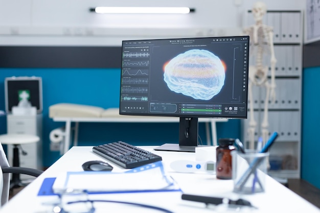 Sala de examen vacía con tomografía cerebral en la pantalla de la computadora lista para consulta de oncología. Habitación de hospital sin nadie equipada con herramientas médicas profesionales. Diagrama de resonancia magnética del cerebro