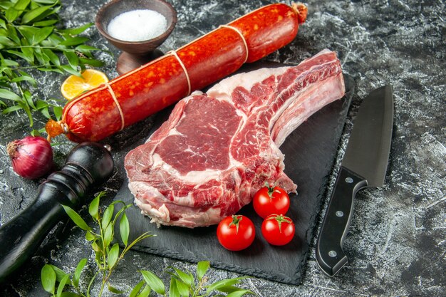 Salchicha fresca de media vista superior con tomates y una rebanada de carne en una superficie oscura clara