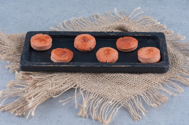 Foto gratuita salchicha frita en rodajas sobre tablero de madera negra.