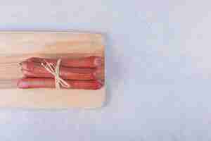 Foto gratuita salchichas ahumadas atadas con cuerda sobre tabla de madera.