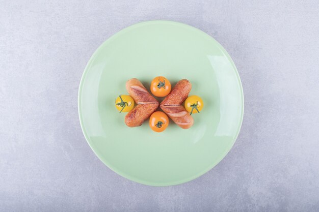 Salchichas fritas y tomates cherry en placa verde.