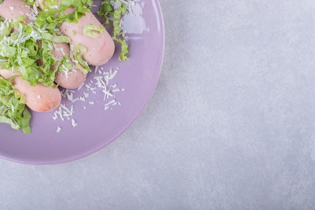 Foto gratuita salchichas hervidas decoradas con lechuga en plato morado.