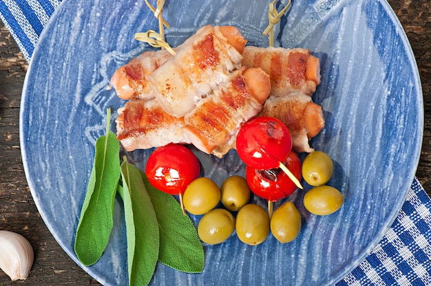 Foto gratuita salchichas a la parrilla envueltas en tiras de tocino con tomates y hojas de salvia