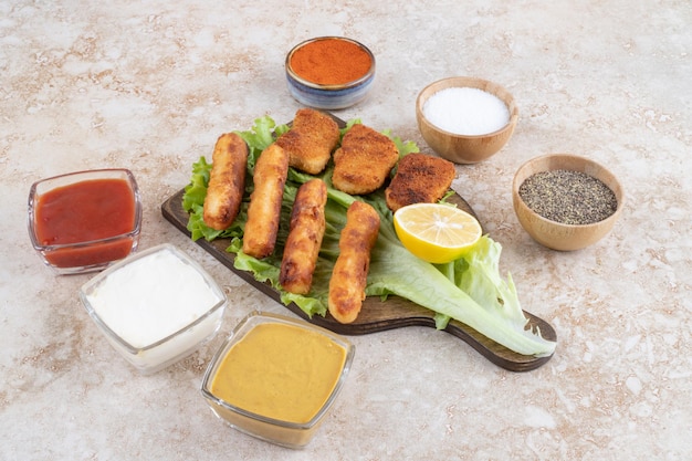 Salchichas a la plancha con nuggets de pollo sobre un trozo de lechuga sobre una tabla de madera con salsas a un lado.