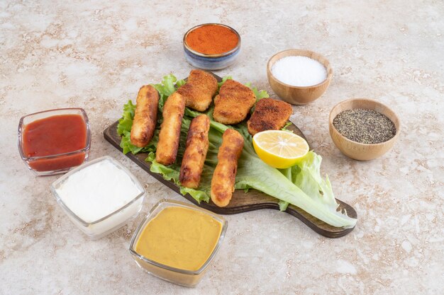 Salchichas a la plancha con nuggets de pollo sobre un trozo de lechuga sobre una tabla de madera con salsas a un lado.