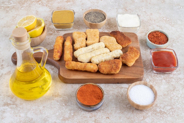 Salchichas a la plancha, palitos de queso y nuggets de pollo con salsas en un plato de madera.