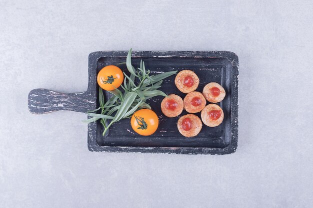 Salchichas en rodajas con salsa de tomate y tomates en tablero negro.