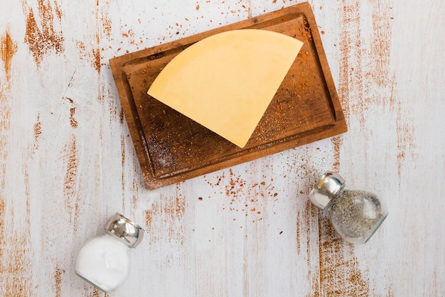 Salero y pimentero negro botellas con queso en la tabla de cortar