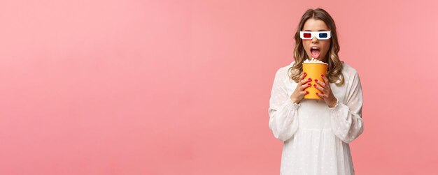 Salida de ocio y concepto de primavera retrato de linda chica rubia divertida en el cine comiendo palomitas de maíz de