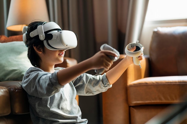 Foto gratuita salir de un niño asiático disfruta de juegos de metaverso con auriculares vr portátiles con manija de control jugando juegos deportivos en línea en la sala de estar en casa tecnología casera joven adolescente usando tecnología vr