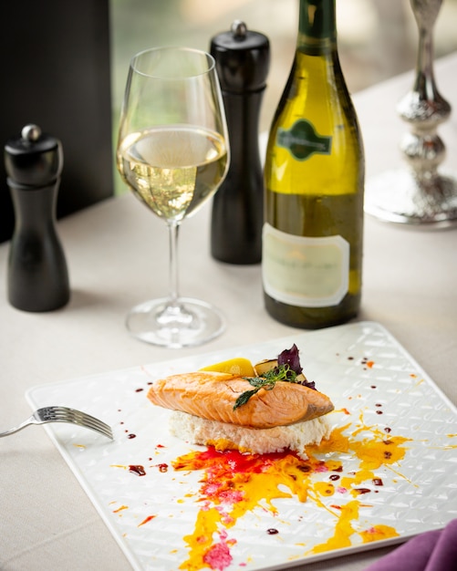 Salmón frito con verduras y una copa de vino blanco.