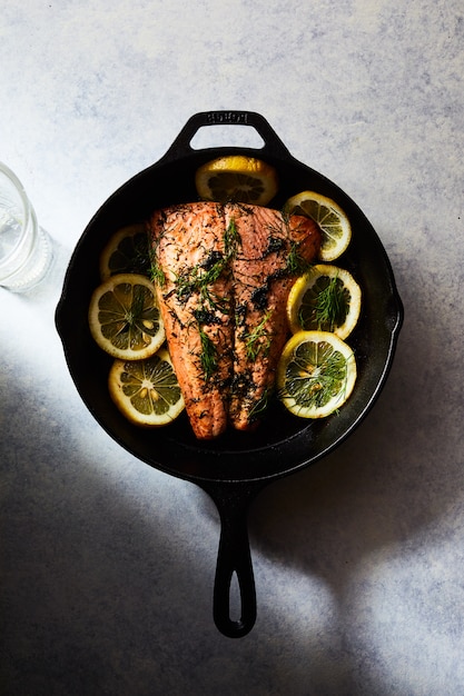 salmón a la plancha con limones en una olla negra sobre una superficie blanca