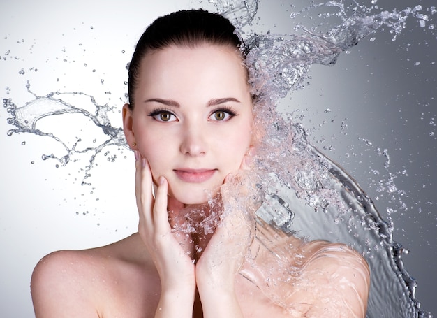 Salpicaduras de agua en el bello rostro de la mujer joven - espacio gris