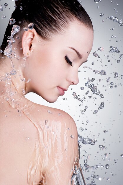 Salpicaduras y gotas de agua alrededor del rostro femenino con piel limpia - vertical