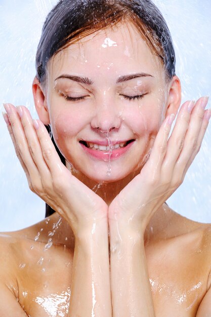 Salpicaduras y gotas de agua en el rostro femenino joven feliz