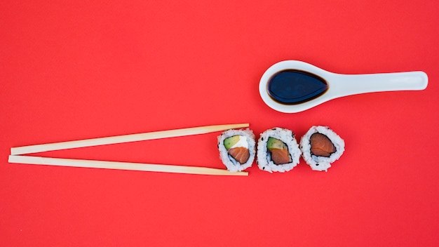 Foto gratuita salsa de soja en cuchara con palillos y sushi sobre fondo rojo