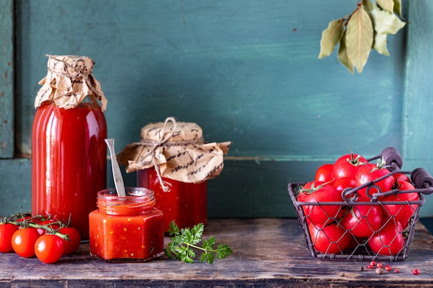 Salsa de tomate casera hecha de tomates rojos maduros en frascos de vidrio con ingredientes sobre una mesa de madera antigua