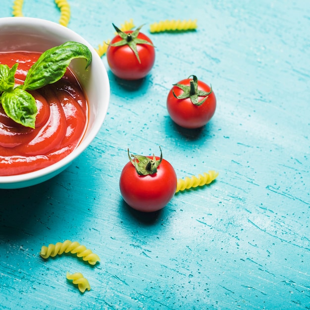 Salsa de tomates con hojas de albahaca y pasta sin cocer sobre fondo de madera