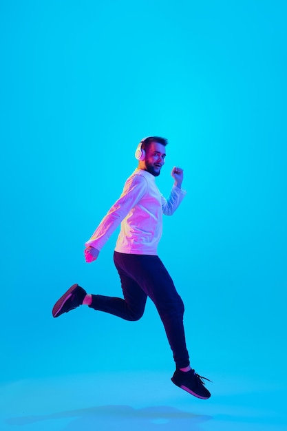 Saltando alto Retrato de un hombre caucásico aislado en un estudio azul con luz de neón. Hermoso modelo masculino. Concepto de emociones humanas, expresión facial, ventas, publicidad. Copyspace para el anuncio. Volantes