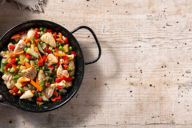 Salteado de pollo y verduras en mesa de madera