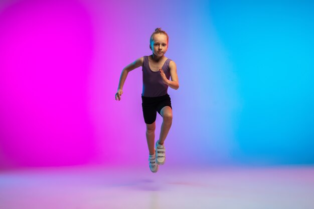 Saludable. Adolescente, corredor profesional, corredor en acción, movimiento aislado sobre fondo rosa-azul degradado en luz de neón. Concepto de deporte, movimiento, energía y estilo de vida dinámico y saludable.