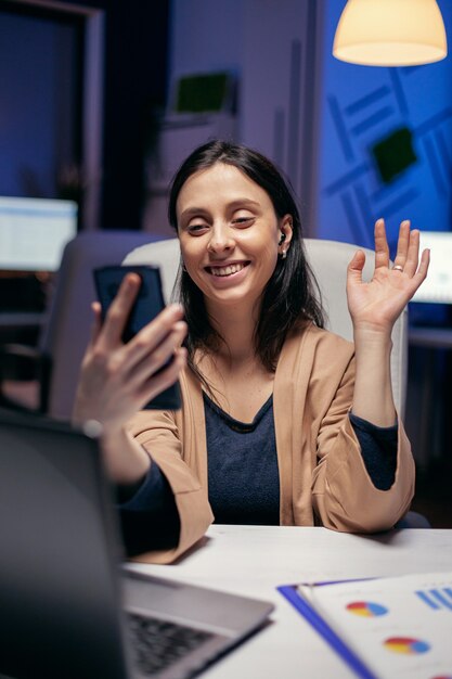 Saludar en el transcurso de la teleconferencia con emprendedores que hacen horas extras. Mujer que trabaja en finanzas durante una videoconferencia con compañeros de trabajo por la noche en la oficina.