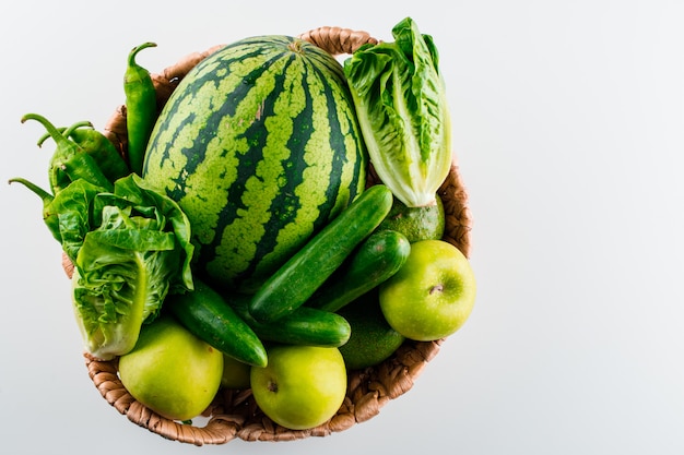 Sandía en una cesta de mimbre con lechuga, manzana, pepino, aguacate, pimientos sobre una mesa blanca